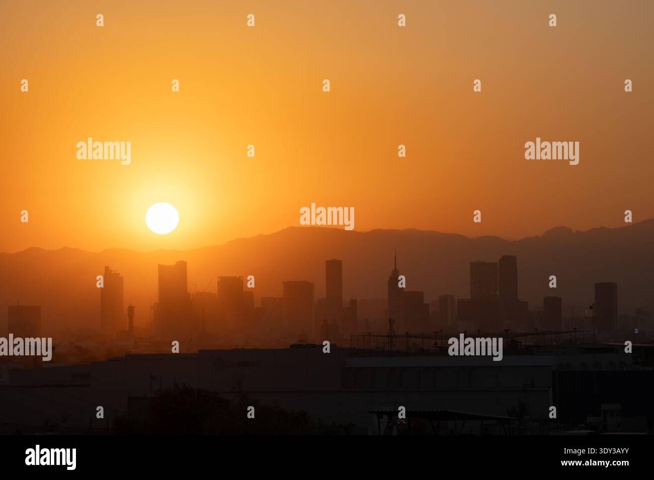 Golden sunset over the silhouetted skyline of Mexico City featuring Torre Latinoamericana and distant mountains in hazy orange light, Mexico. Stock Photo