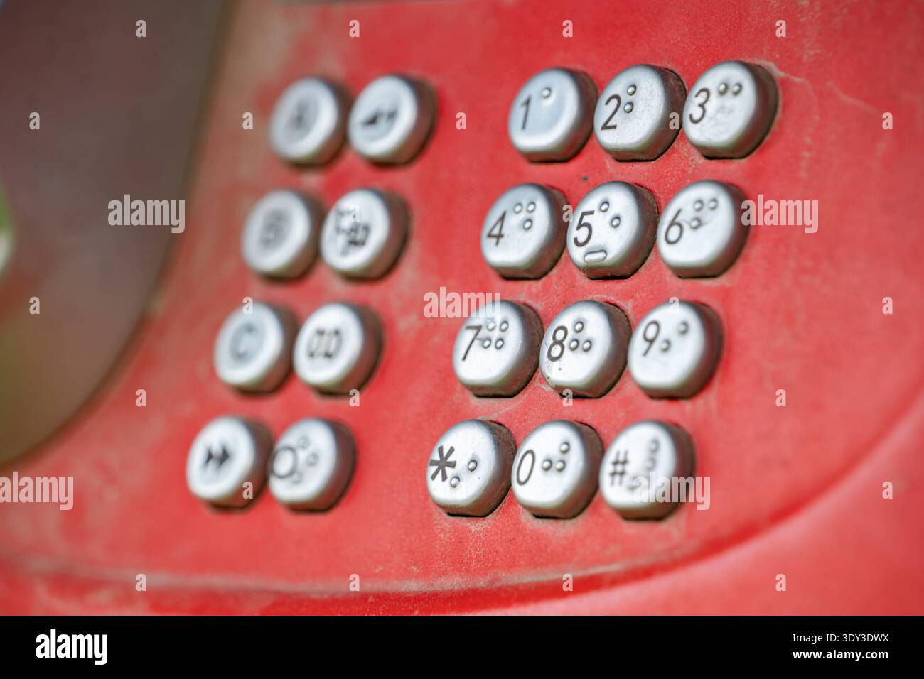 Close-up of dusty red payphone keypad with metal buttons, numbers 
