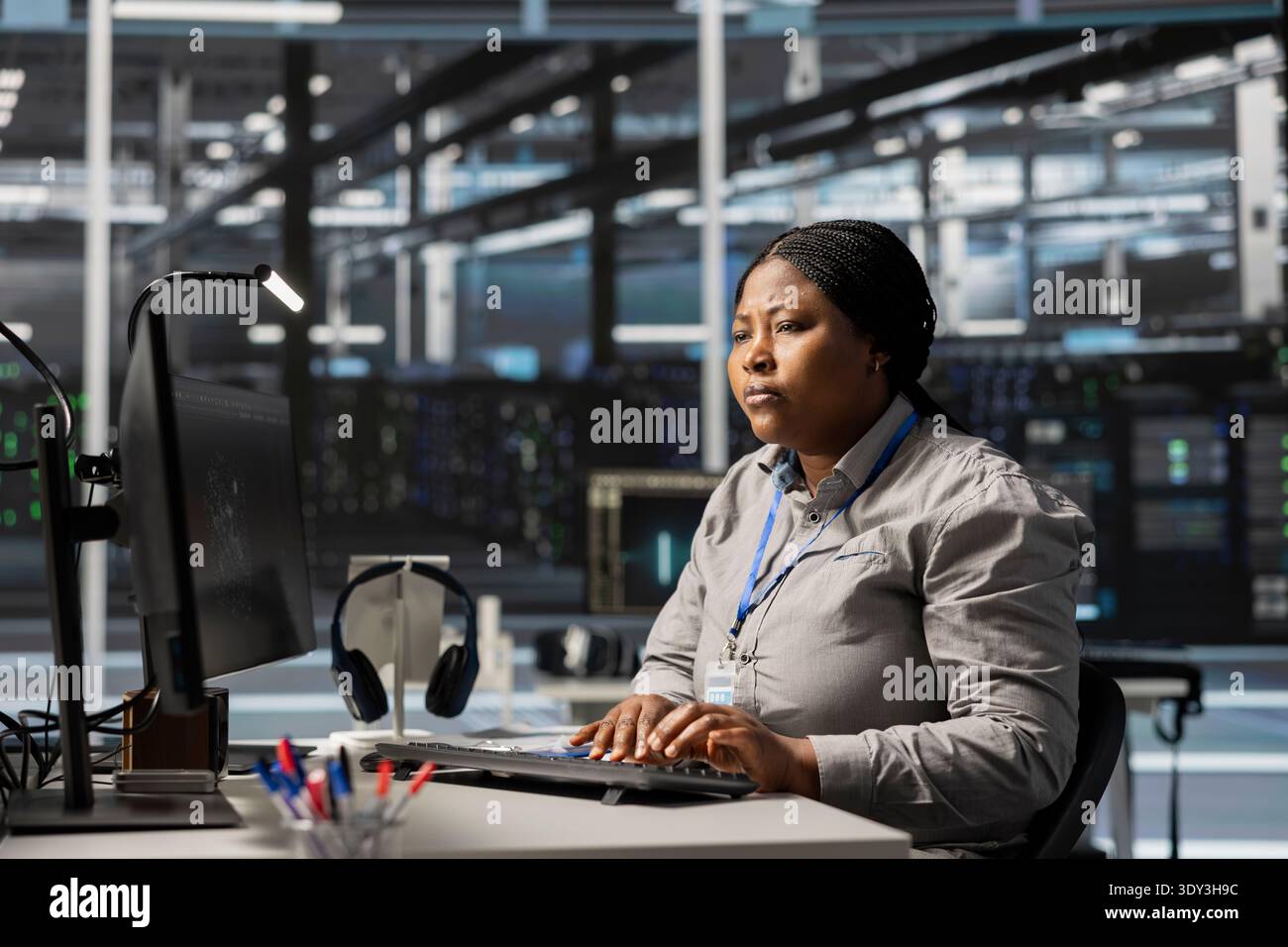 Data center software developer uses PC to update servers tech, configuring gear using program. Woman working in server farm reviewing hardware analytics, ensuring reliable network operations Stock Photo