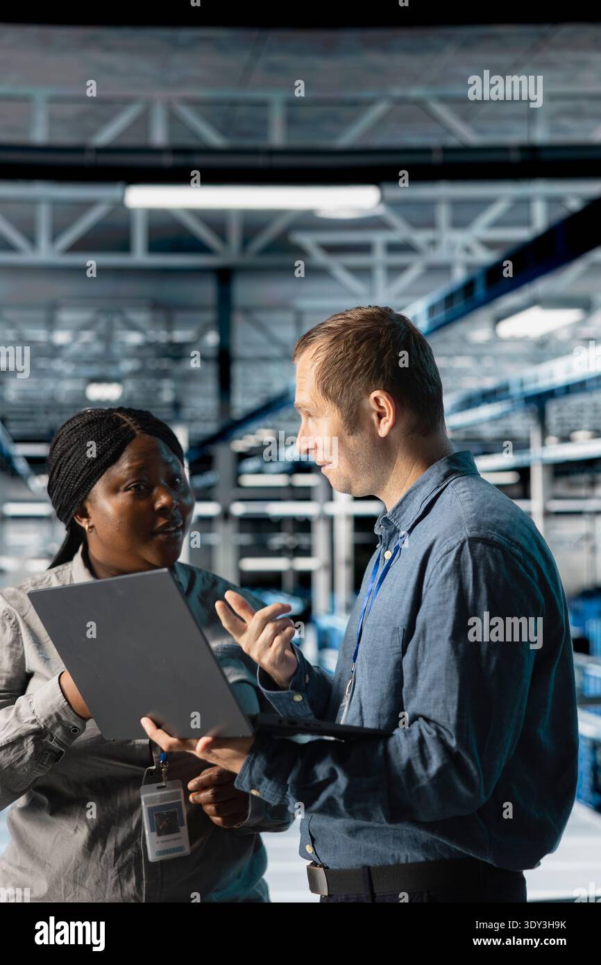 Server room coworkers troubleshooting server connectivity issues using software on notebook. Teamworking data center technicians upgrading enterprise networks hardware using laptop Stock Photo