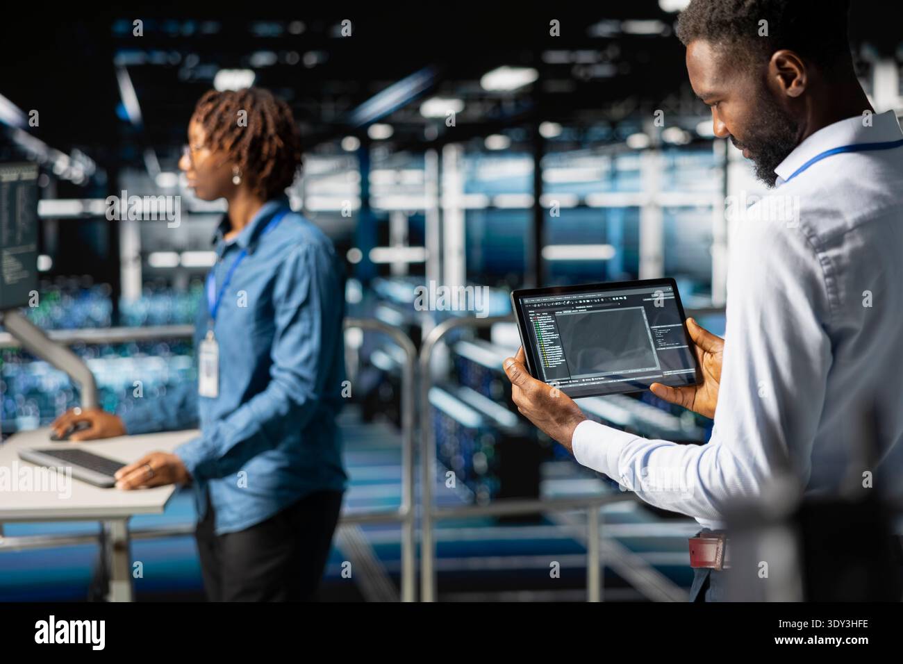 Server room IT programmer visualizing large language model infrastructure using tablet on elevated industrial platform. Data center system administrators collaborating on tasks. Stock Photo