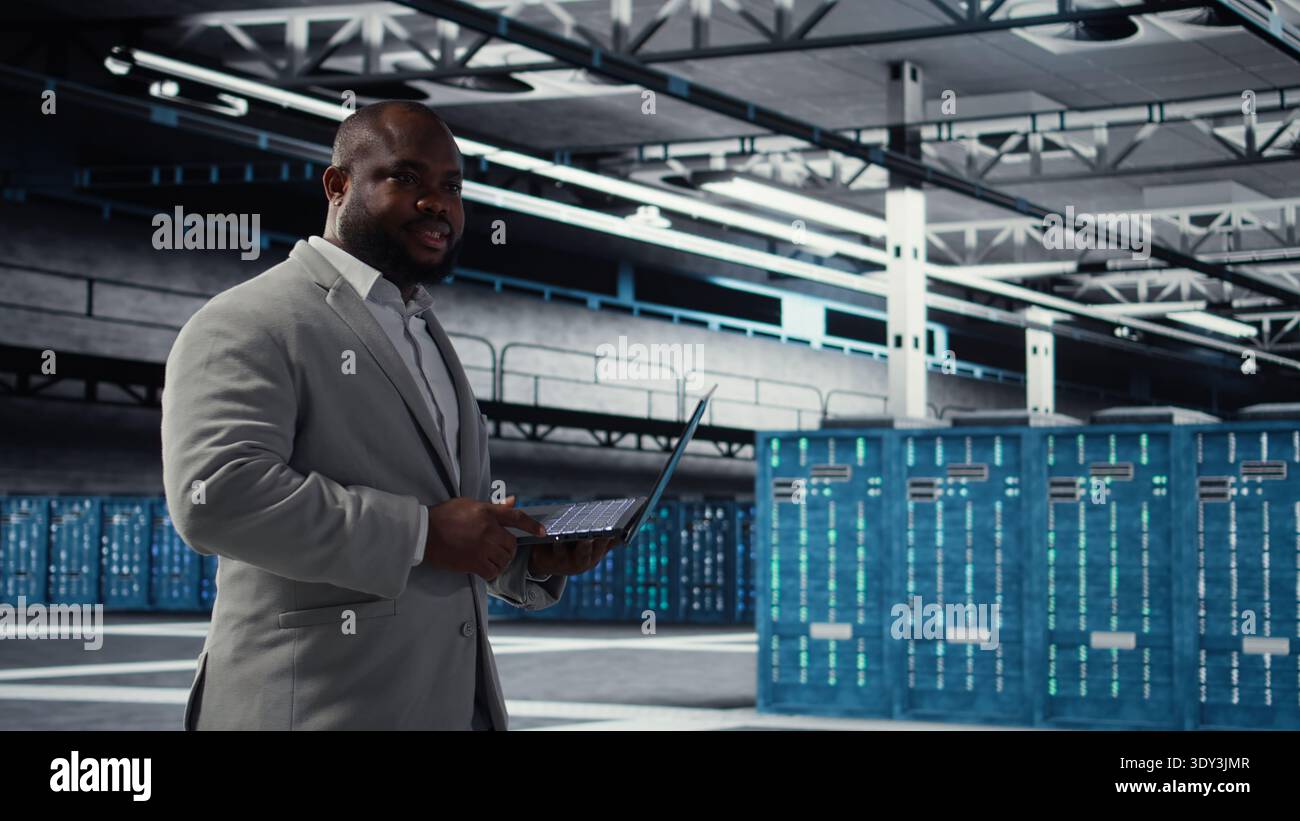 Cheerful data center system administrator reviews code for automation scripts. Jolly server room employee running diagnostics on equipment, doing predictive error detection, camera A Stock Photo
