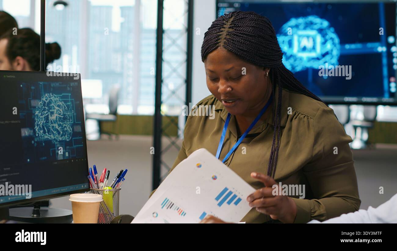 Joyous technician with disability and coworker chatting while coding AI algorithms debugging software issues. Upbeat tech startup office IT expert in wheelchair and colleague using computer, camera A Stock Photo