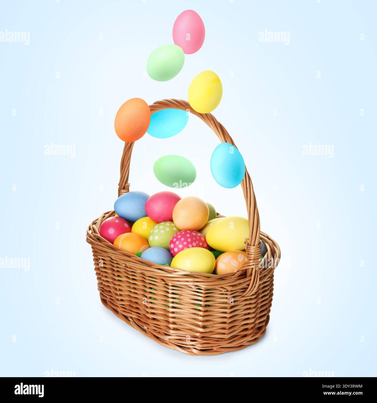 Color Easter eggs falling into basket on light blue gradient background Stock Photo