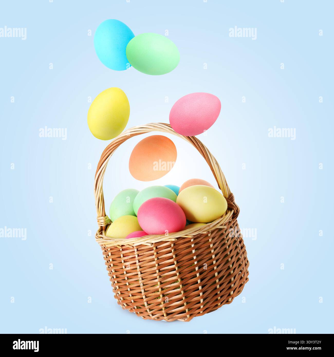 Color Easter eggs falling into basket on light blue gradient background Stock Photo