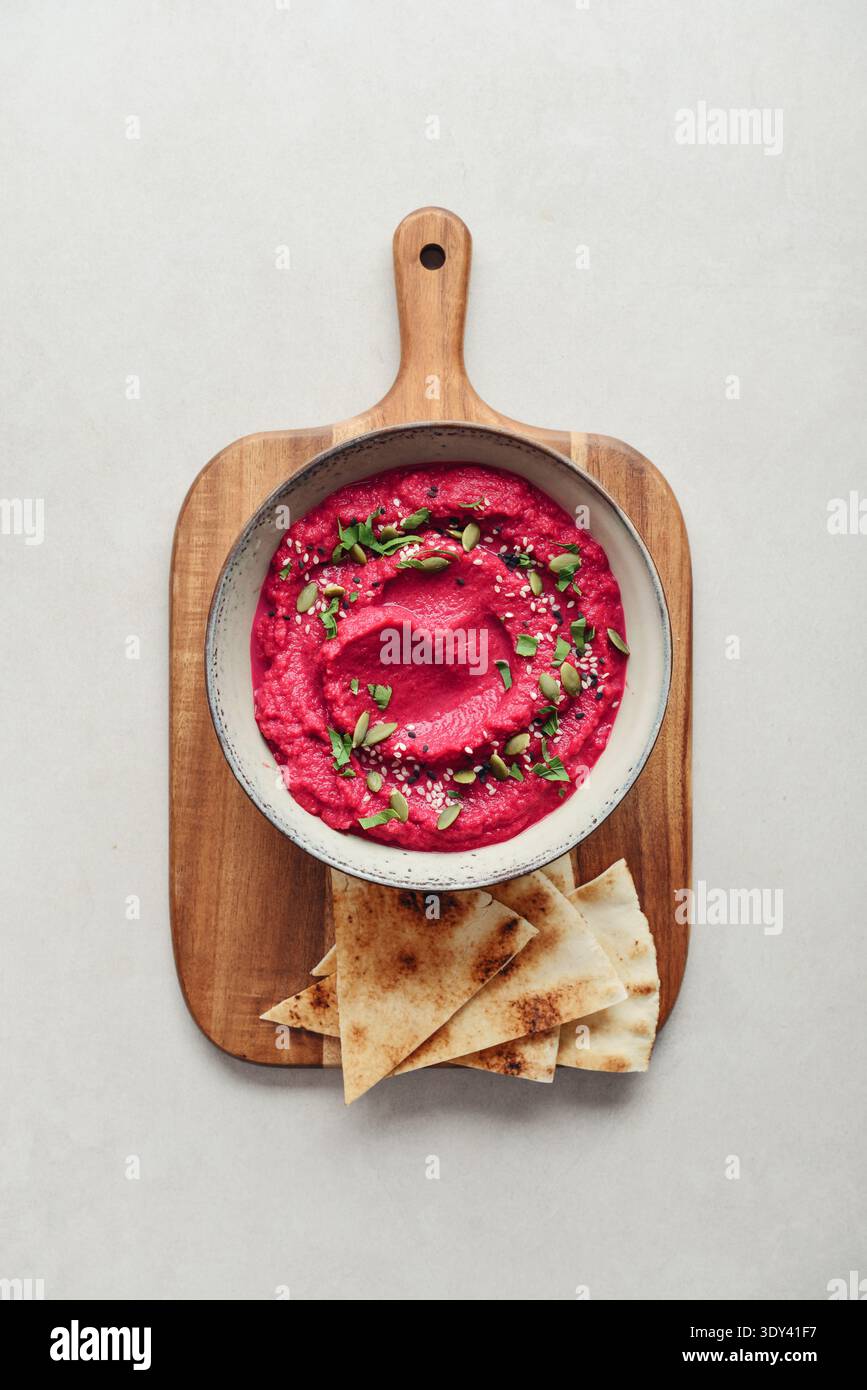 Beetroot hummus decorated with sesame and pumpkin seeds  in bowl with pita bread on gray stone background, top view Stock Photo
