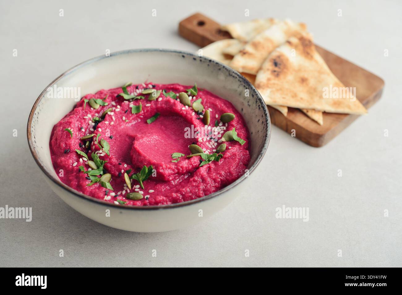 Beetroot hummus decorated with sesame and pumpkin seeds  in bowl with pita bread on gray stone background, top view closeup Stock Photo