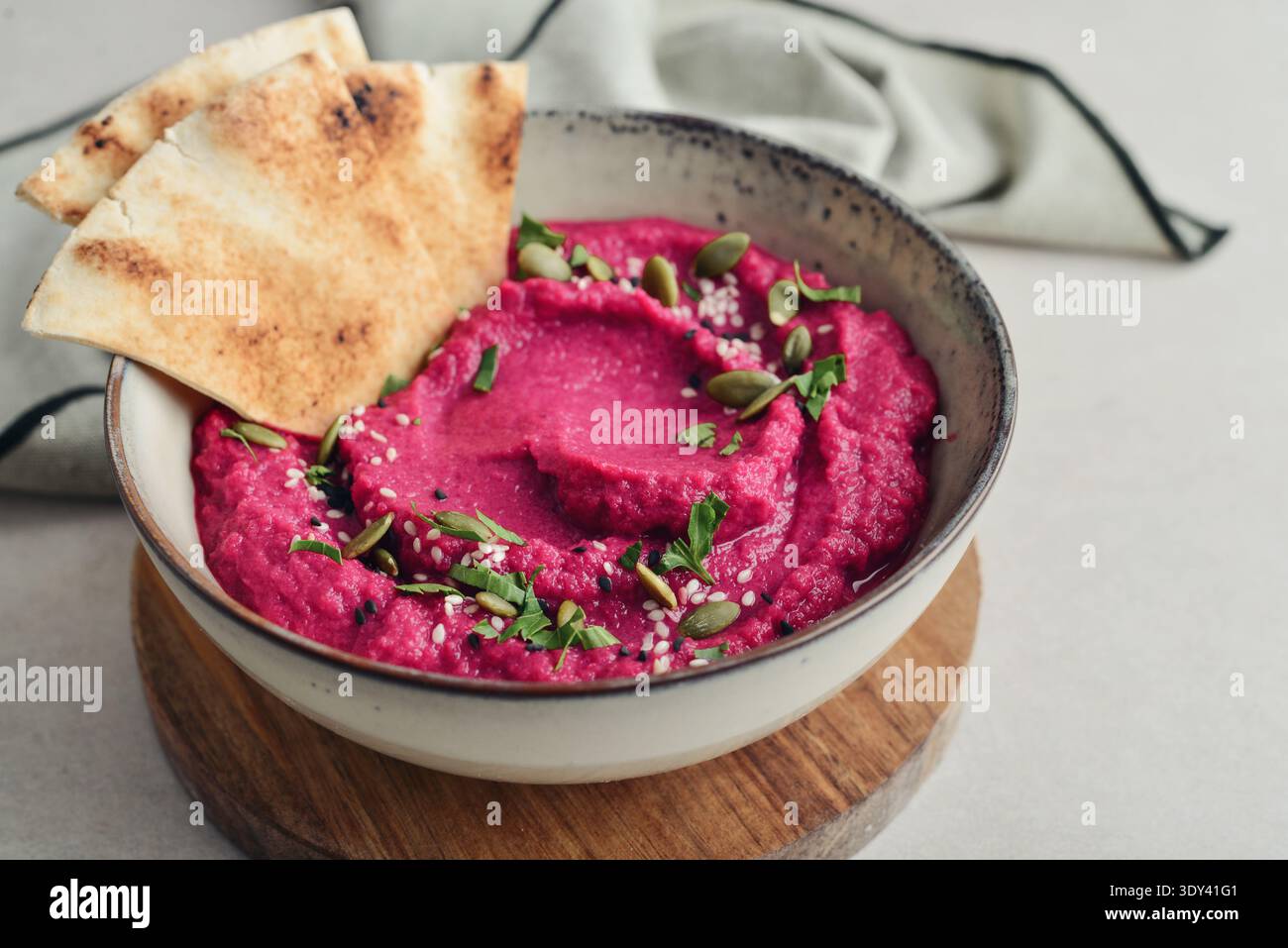Beetroot hummus decorated with sesame and pumpkin seeds  in bowl with pita bread on gray stone background, closeup Stock Photo