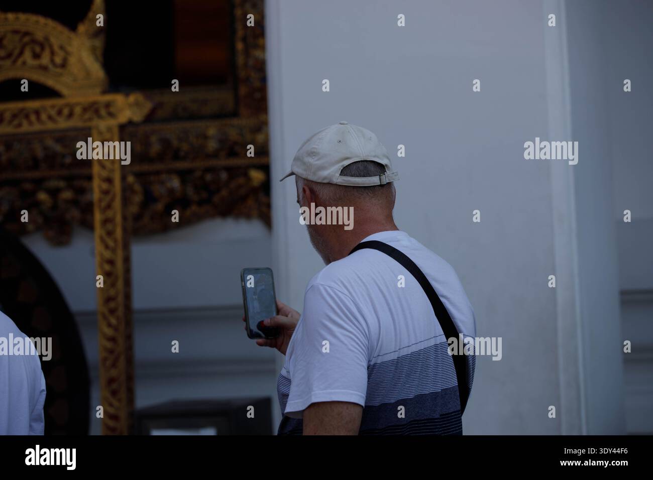Senior man using smartphone taking photo in temple, nonverbal communication, tourists capturing travel moments with smartphone, rear view, at Wat Pho. Stock Photo