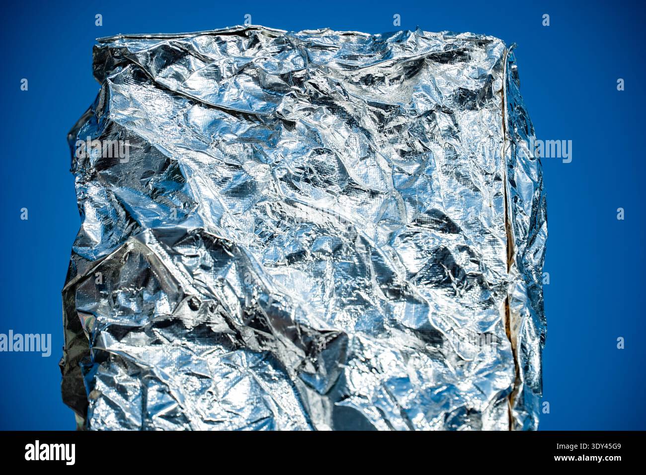 Crumpled aluminum foil surface texture shimmering in sunlight against blue background Stock Photo