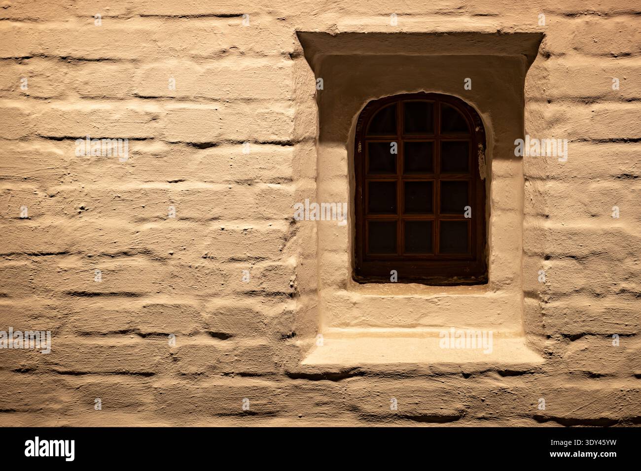 Grungy brick wall with small arched window providing old rustic architecture Stock Photo
