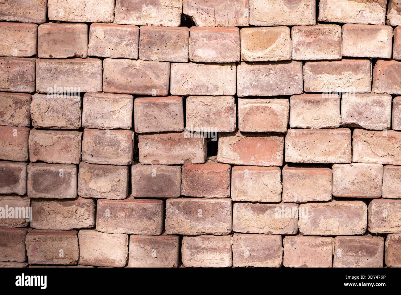 Stacked weathered common bricks forming a textured wall or pavement background Stock Photo