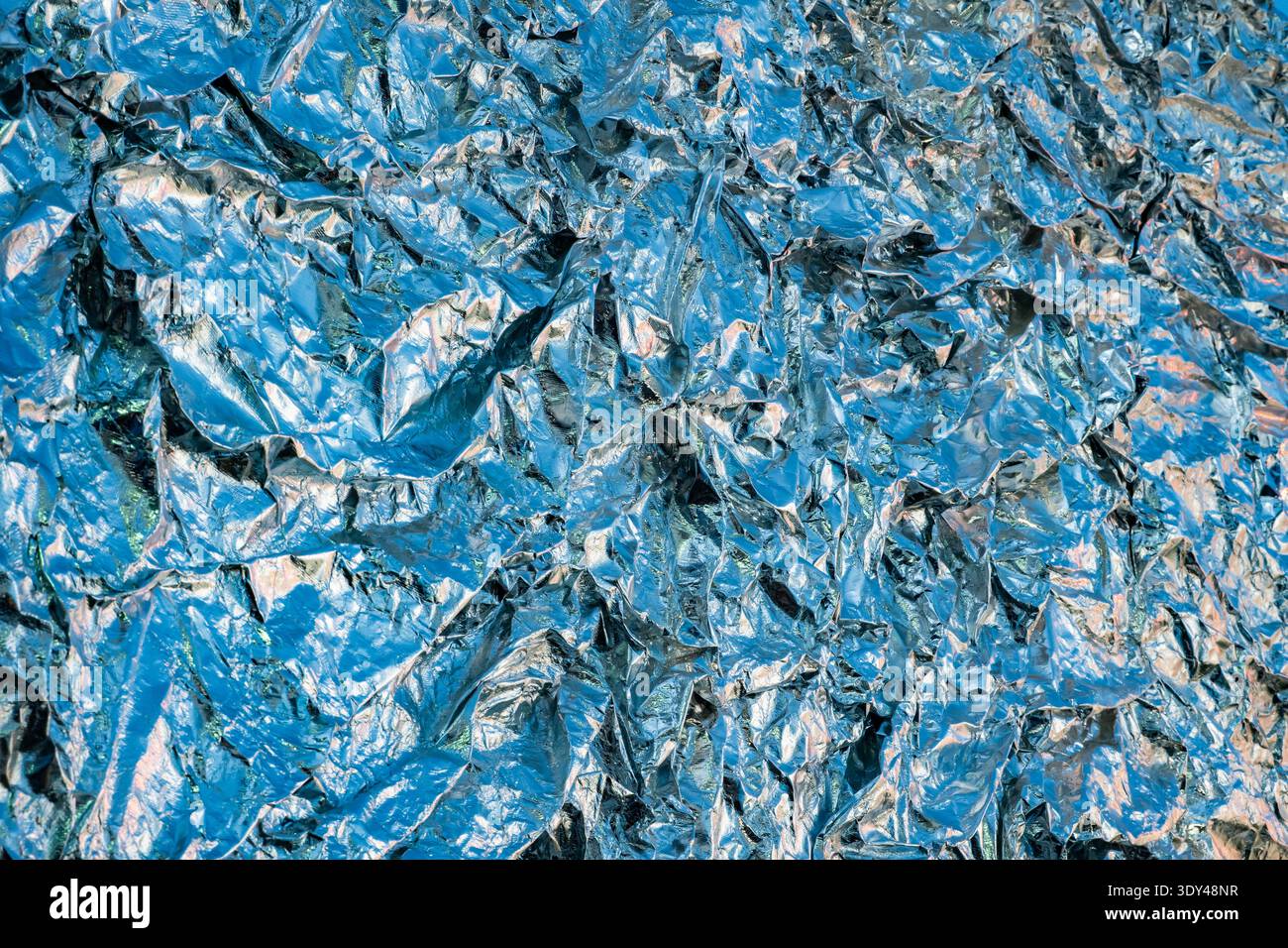 Shiny crumpled blue metallic foil reflecting light creating an abstract texture background Stock Photo