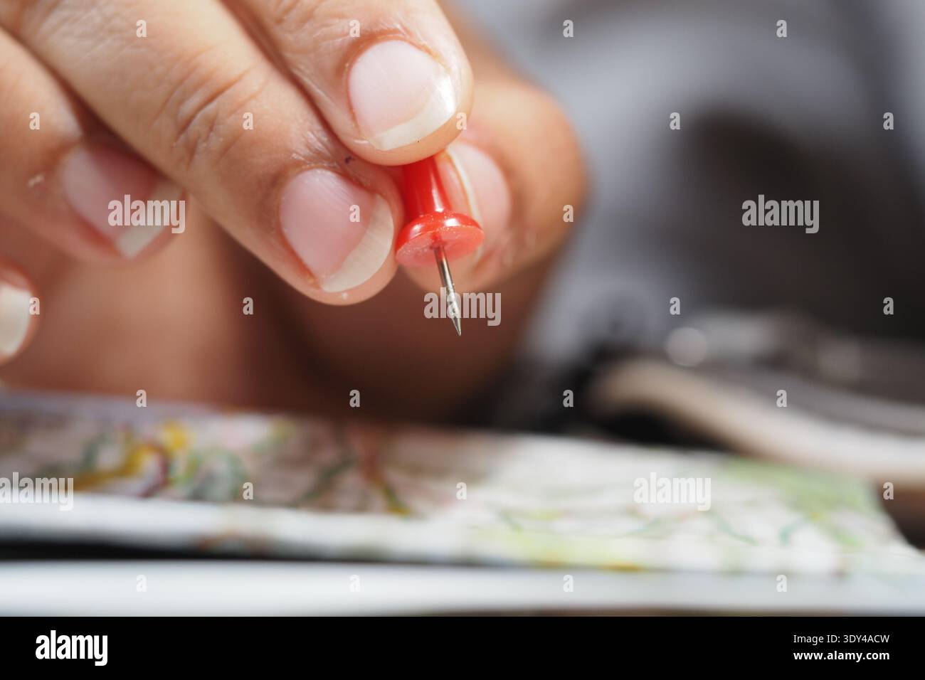 Holding a red push pin above a map on the table Stock Photo