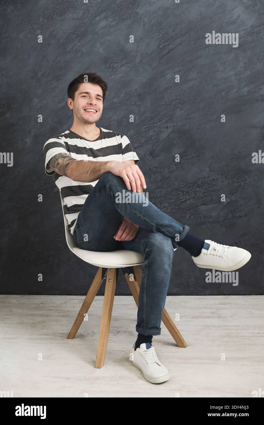 Young smiling man sitting at gray studio background Stock Photo