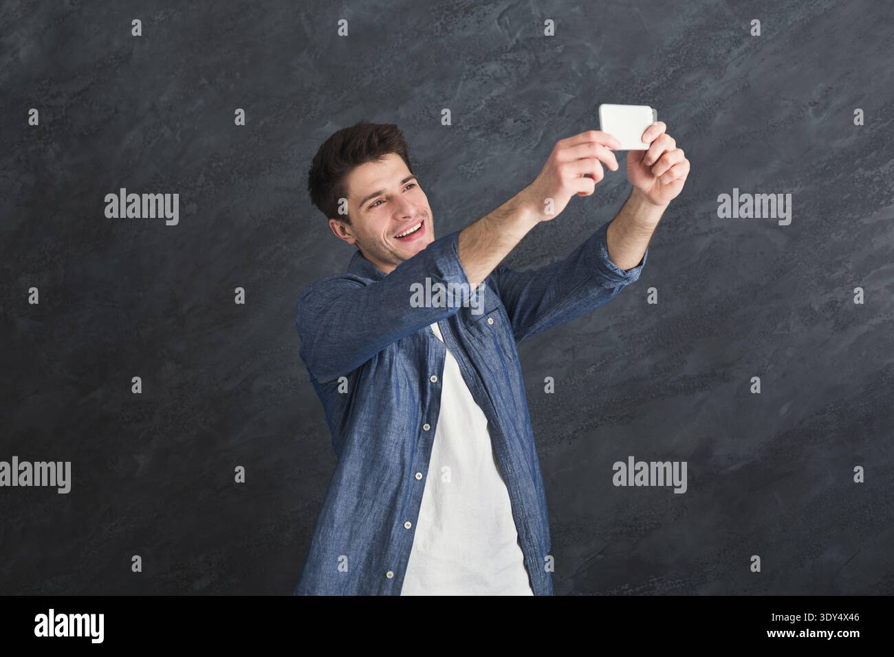 Young man taking selfie on smartphone at gray background Stock Photo