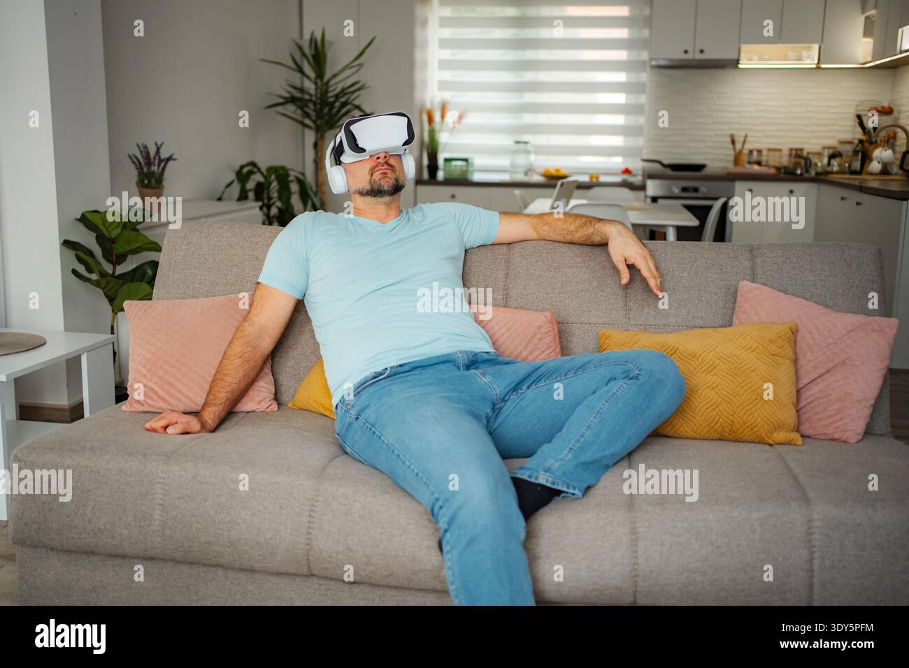 Man wearing VR headset relaxing on sofa at home Stock Photo