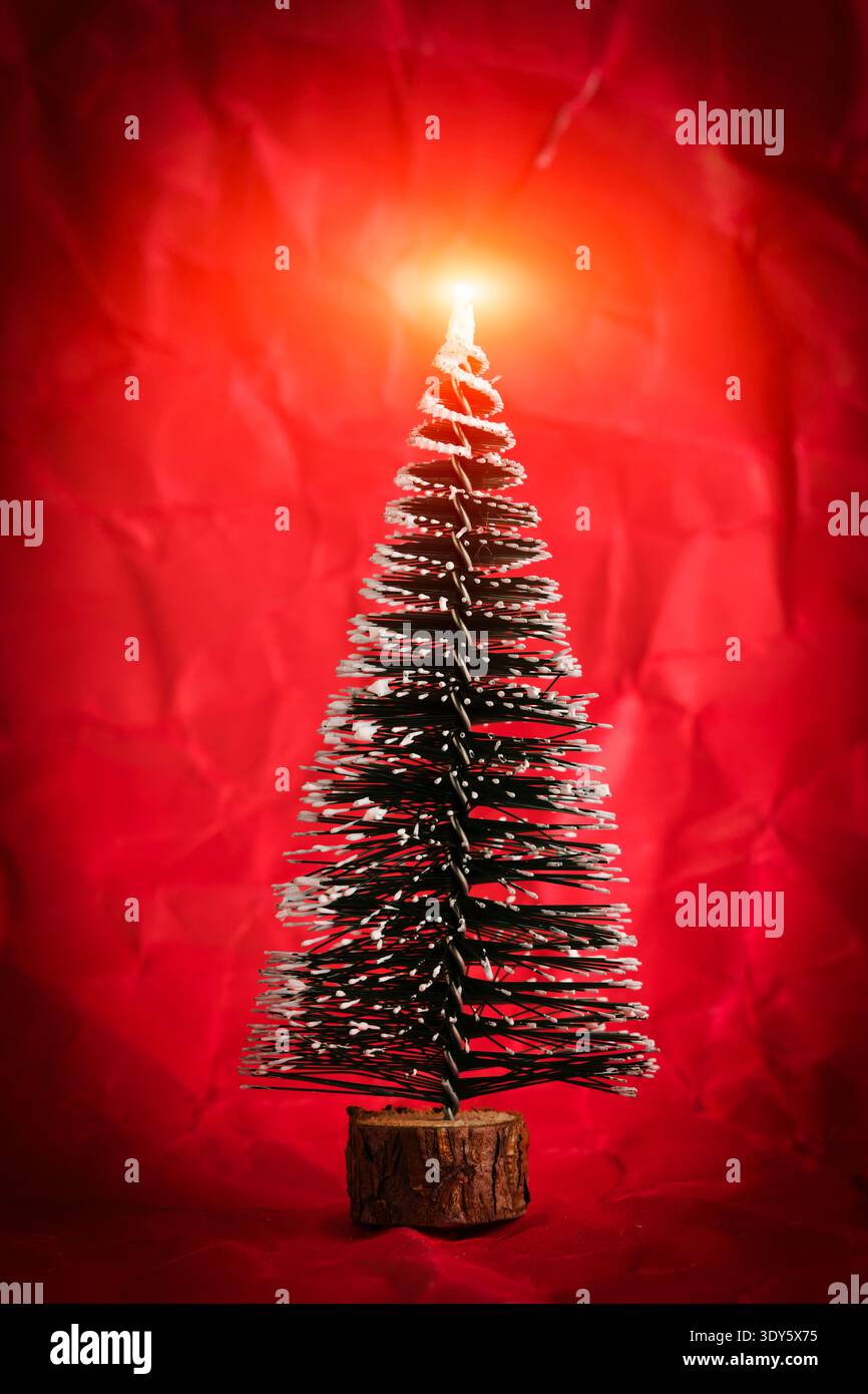 Small snowy Christmas tree with bright glowing star on top on red background. Holiday concept Stock Photo