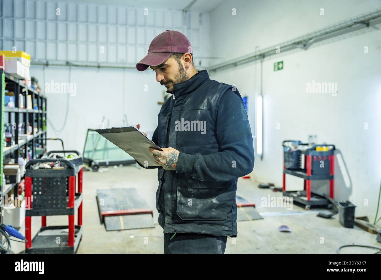 Mechanic in cap and vest inspects vehicle damage in an auto repair ...
