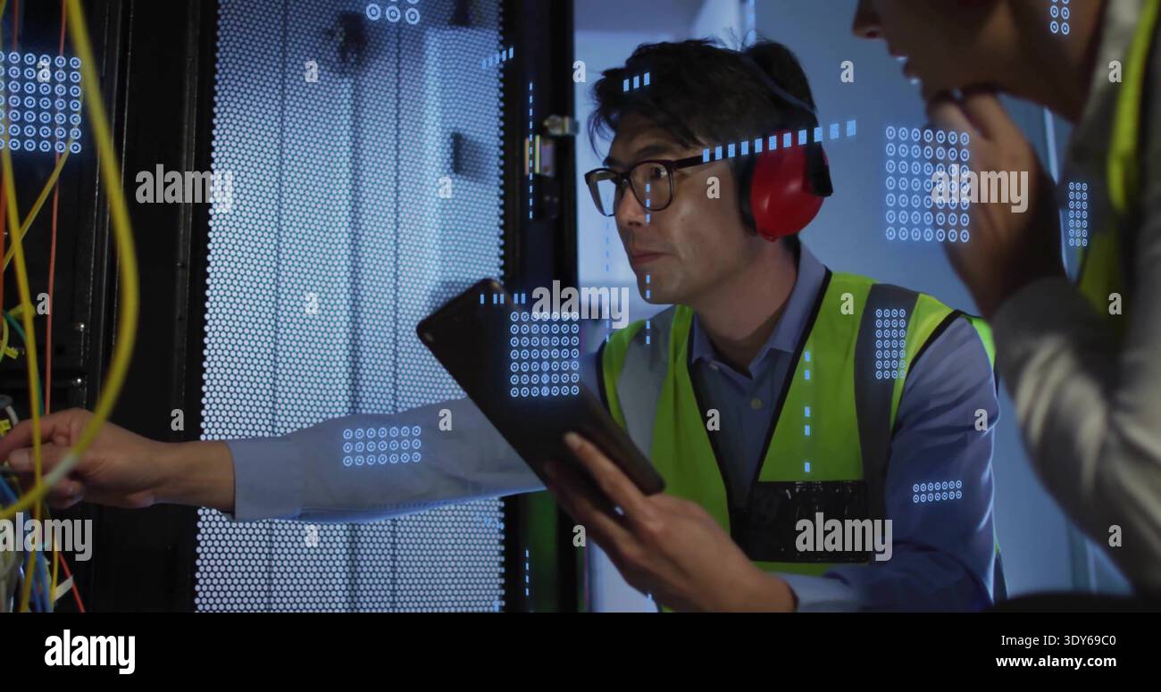 Inspecting Asian tech using tablet and leaning into server rack in data center, yellow cables Stock Photo