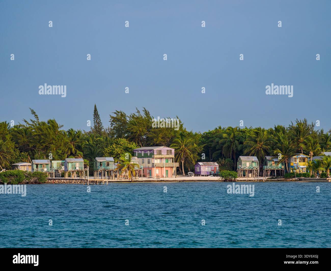 Colorful houses line the waterfront in Caye Caulker as water reflects the clear sky in Belize District Stock Photo