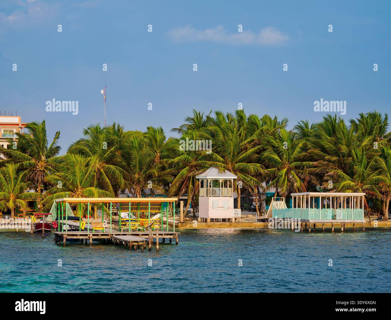 Visitors enjoy the waterfront area with palm trees and cabanas in Caye Caulker Belize during a sunny day Stock Photo