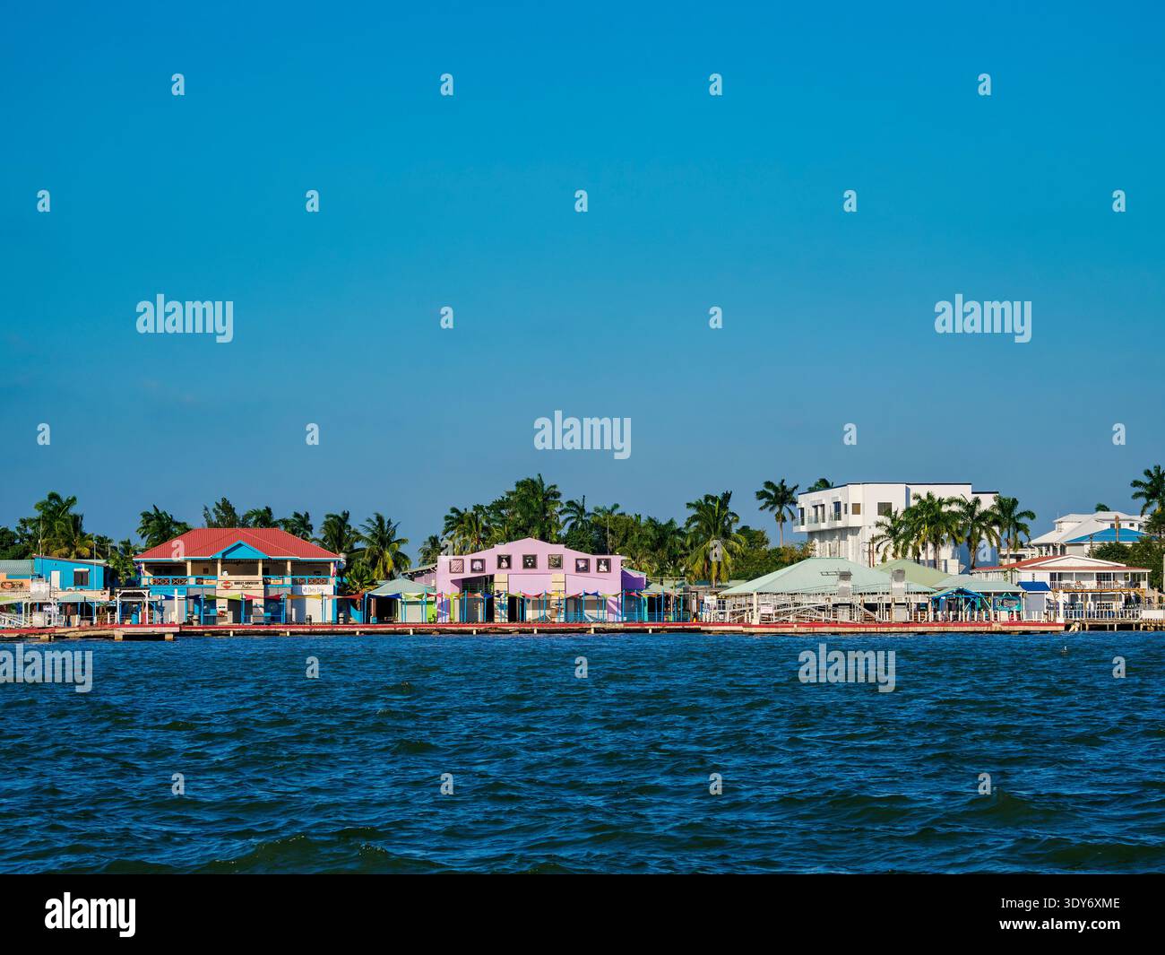 Vibrant waterfront area of Belize City with colorful buildings and palm trees by the water in Belize District Stock Photo