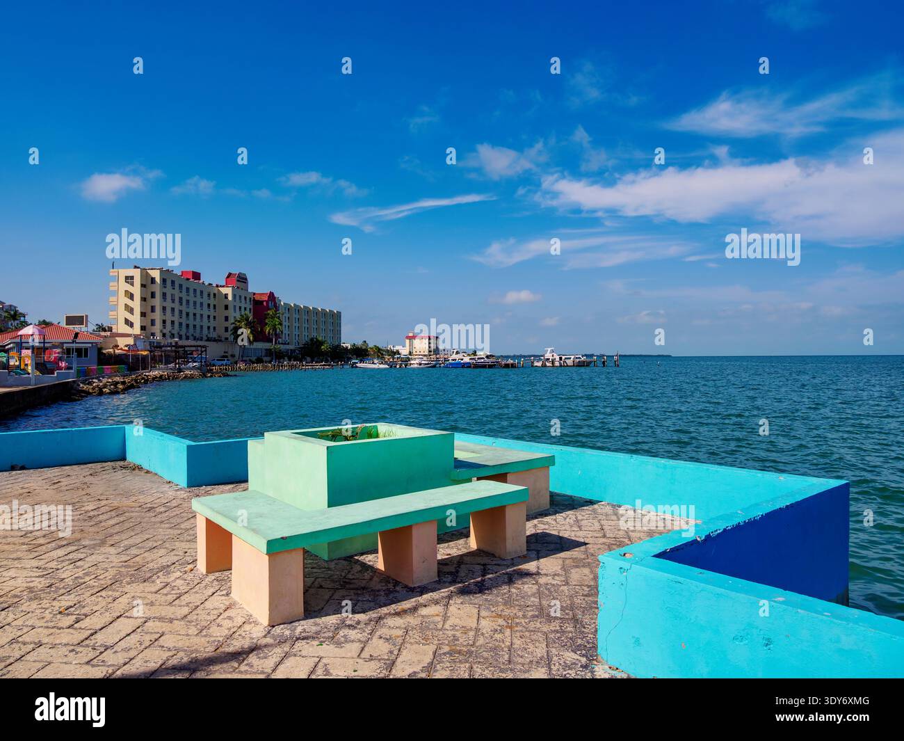 Colorful benches along the waterfront overlook the sea and buildings in Belize City, situated in the Belize District of Belize Stock Photo