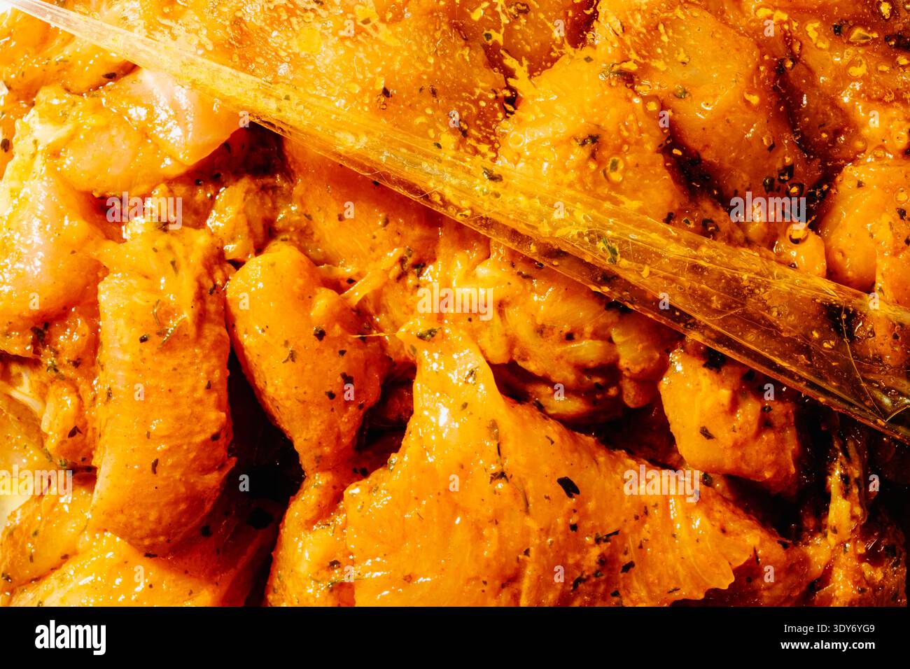 closeup of seasoned raw chicken pieces marinating inside a transparent plastic bag, covered with spices and oil, preparation of meat before cooking in Stock Photo