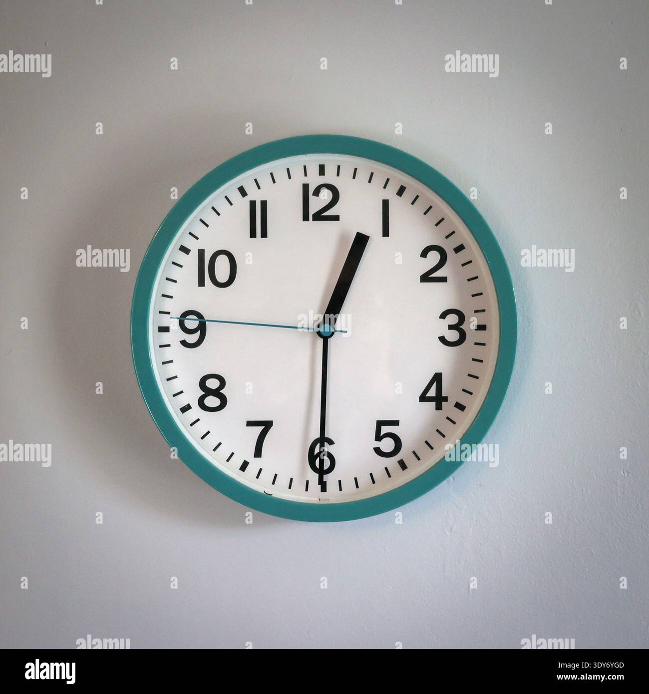 A cheap turquoise wall clock with white clock face, showing the hands at twelve thirty pm , hanging on wall in a house. Stock Photo