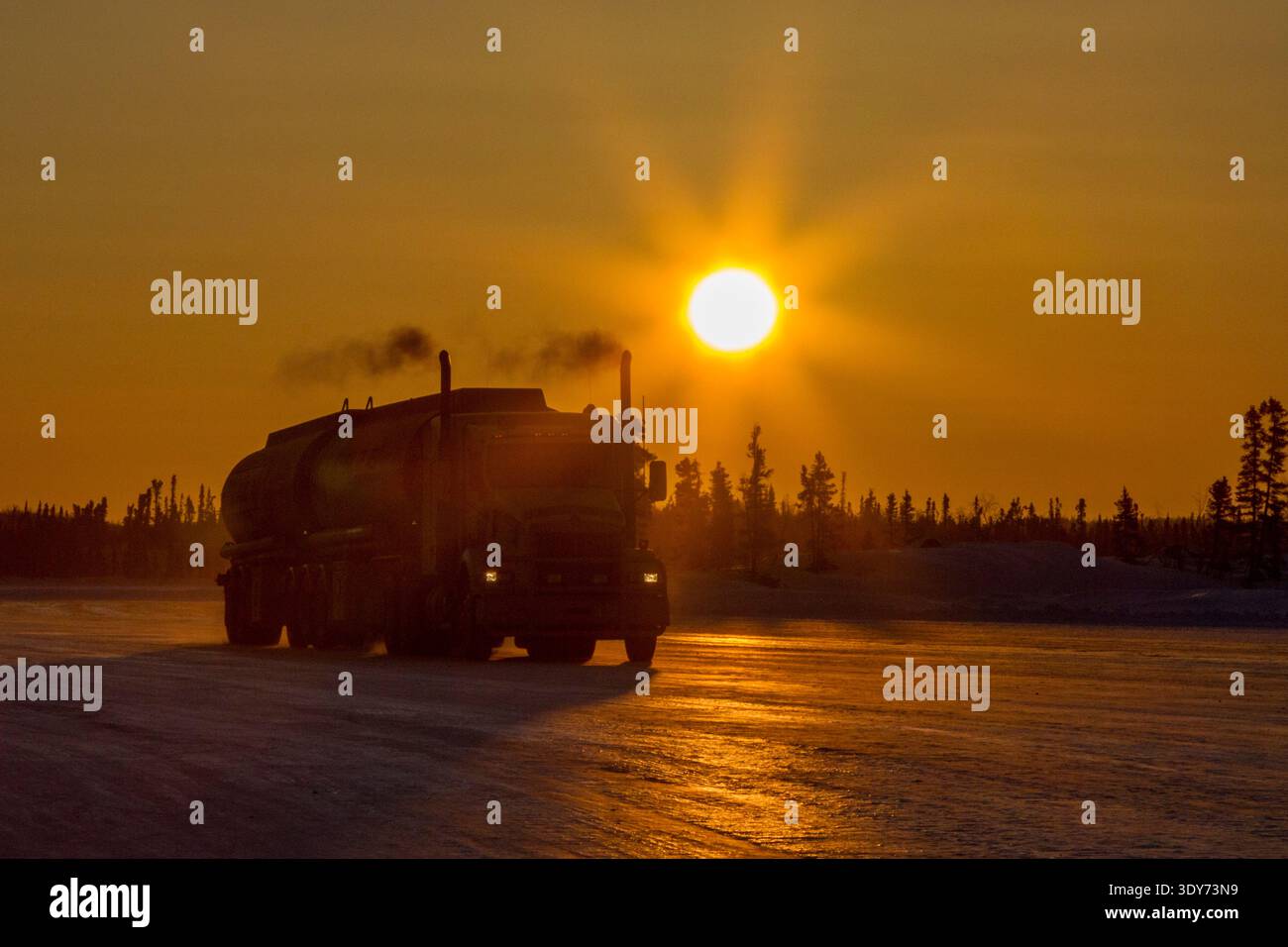 Heavy trucks travel on ice road at sunset on frozen lake in Northwest Territories Canada Stock Photo