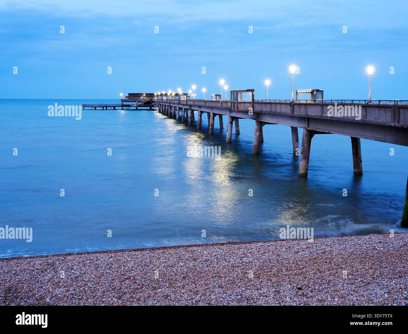 Dusk settles over a well-lit pier extending into the sea in Deal Kent offering views and a sense of evening activity Stock Photo