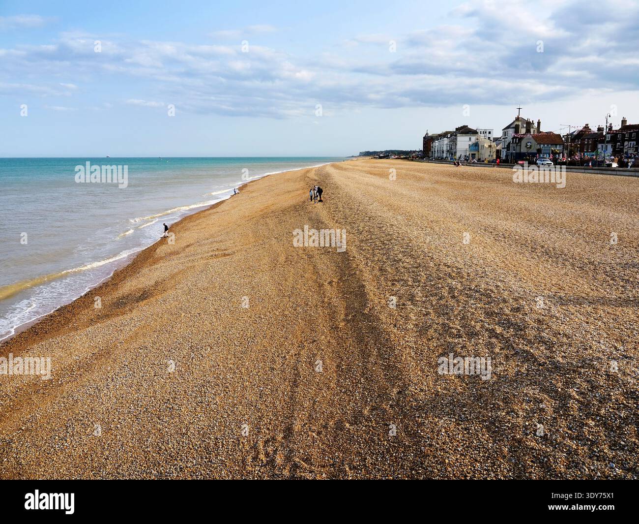 Sunny day at the beach from the pier with people walking along the shore in Deal, Kent, United Kingdom Stock Photo