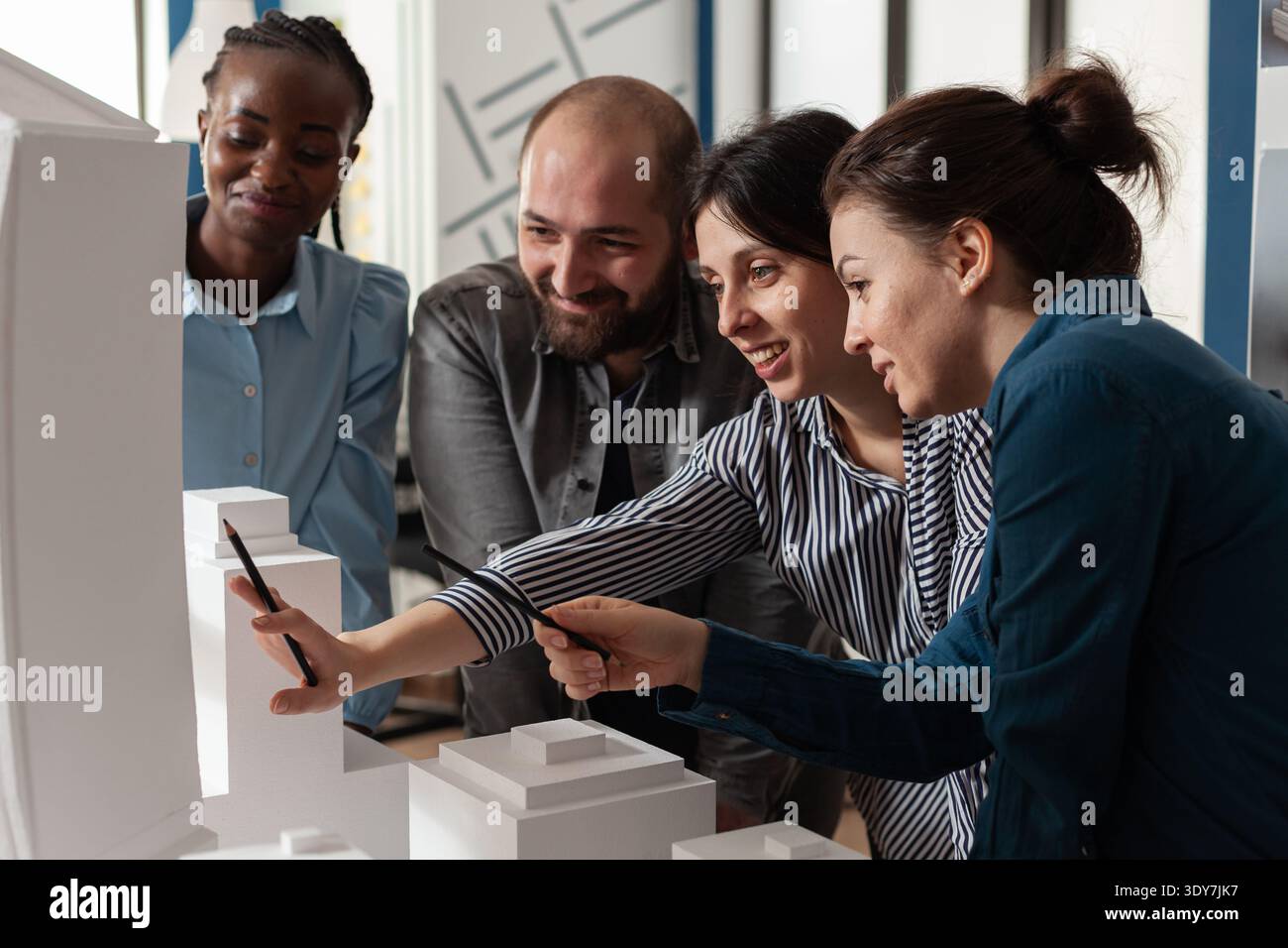 Multi ethnic architectural teamwork analyzing maquette building model construction layout. Diverse professional group of colleagues pointing at project design blueprint plan Stock Photo