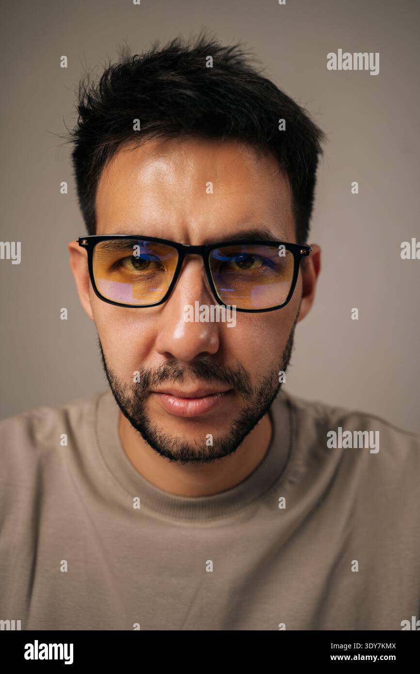 Close-up vertical portrait of young man wearing anti-fatigue glasses with focused and concerned expression, showcasing deep thought and concentration Stock Photo