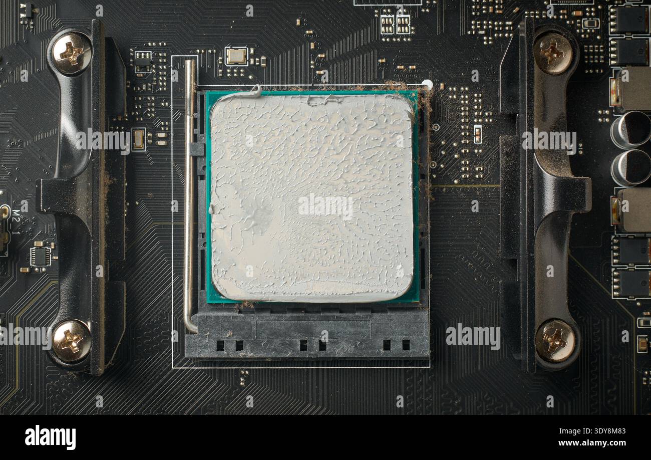 used computer motherboard and installed cpu covered in grey thermal paste, textured compound surface in full frame in top view, pc maintenance concept Stock Photo