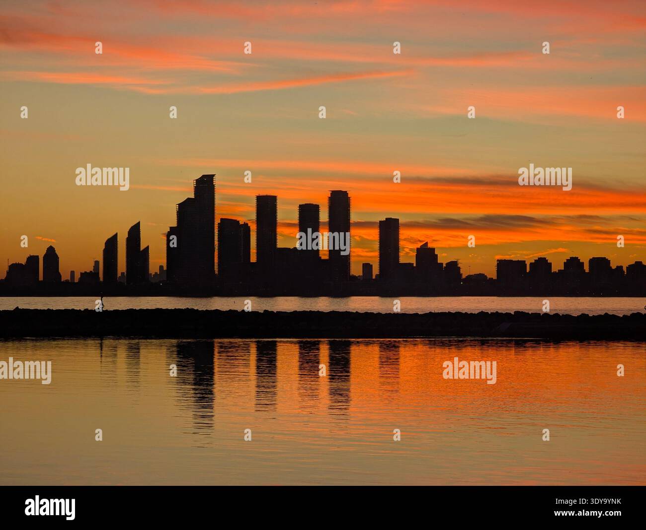 Vibrant orange sunset over a modern city skyline, reflected in tranquil water at dusk. Perfect for travel or editorial use. - Smartphone Captured Stock Image