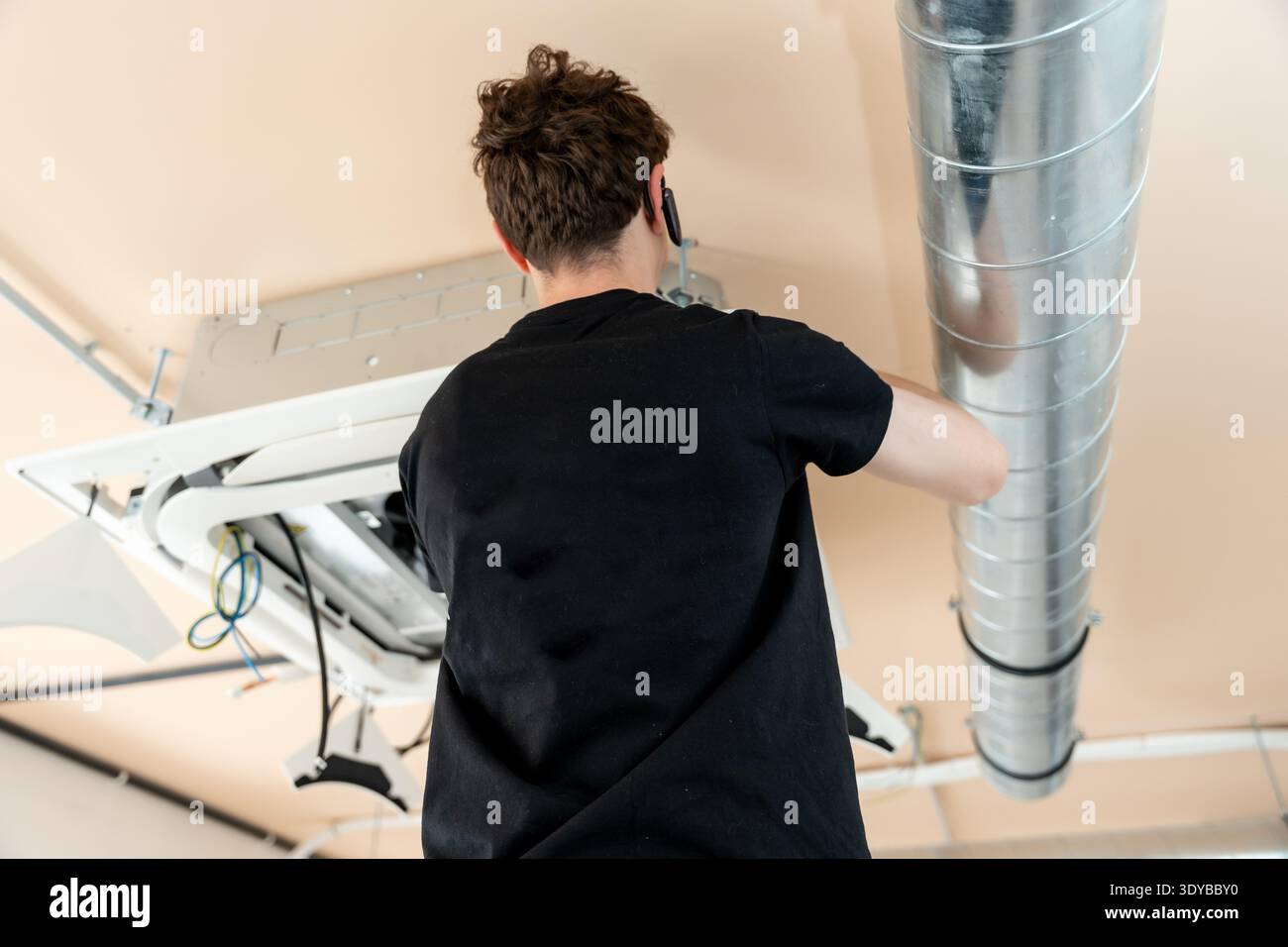 Technician installing air conditioning ceiling unit and ductwork Stock Photo
