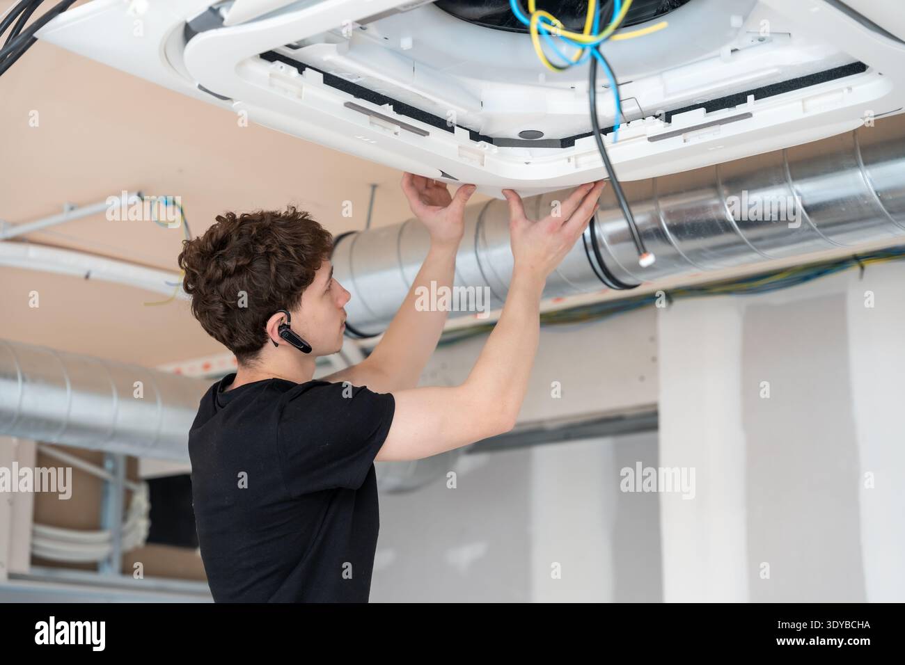 Technician installing ceiling air conditioning unit during construction Stock Photo