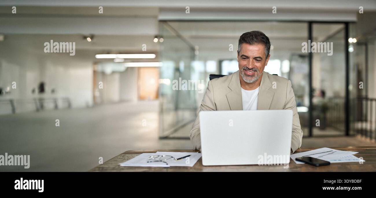 Happy middle aged professional business man using computer working at desk. Stock Photo