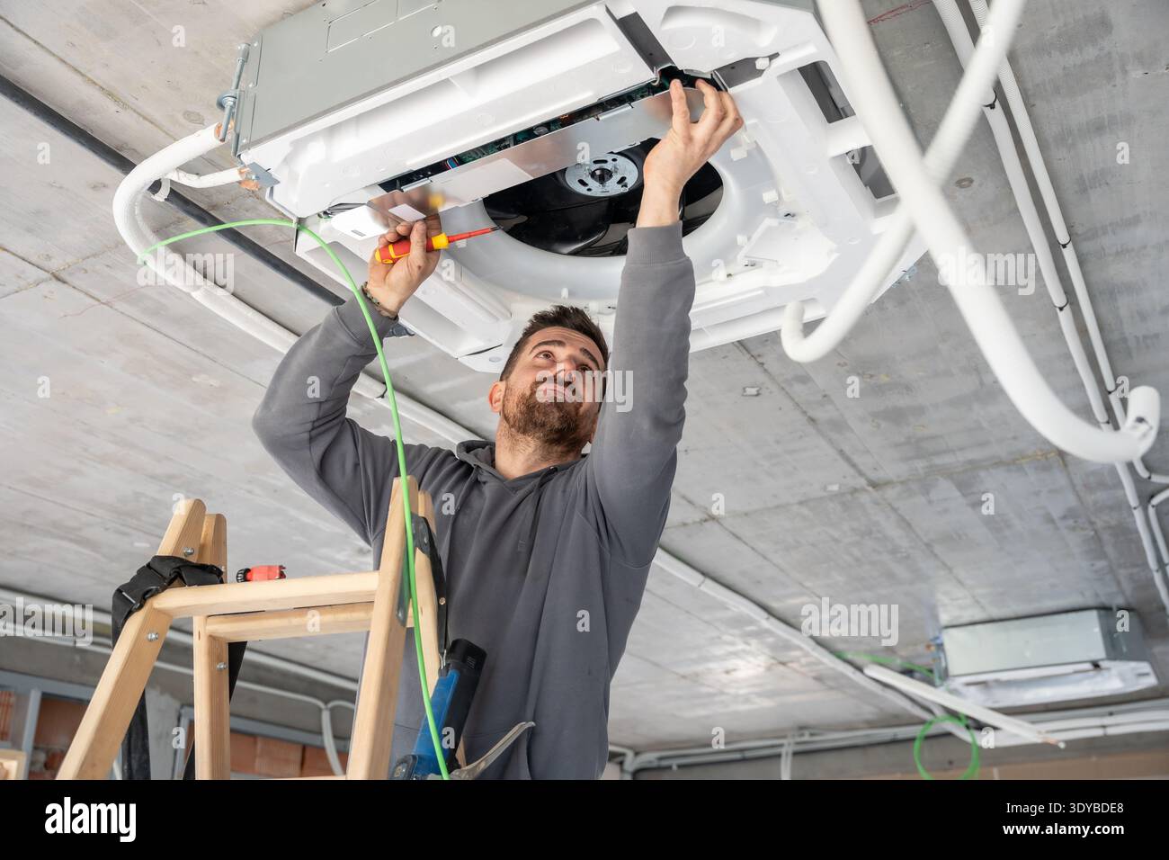 Air conditioning technician installing ventilation system on a building ceiling Stock Photo