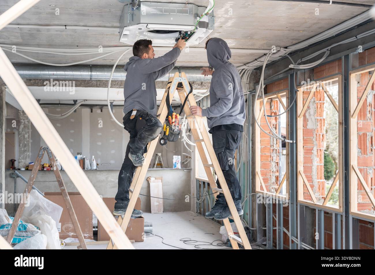 Technicians installing air conditioning unit on construction site Stock Photo
