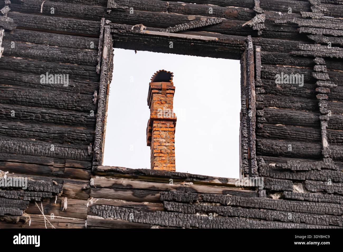Charred log house wall with brick chimney seen through a window frame Stock Photo