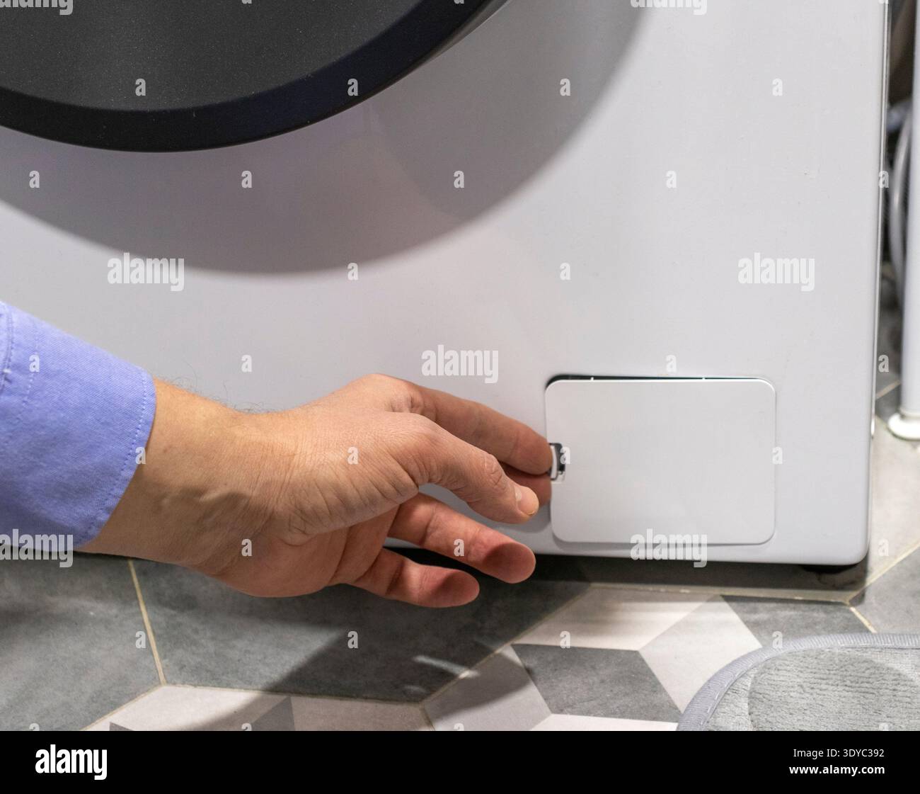 Man opening the drain pump filter access panel of the front loading washing machine Stock Photo