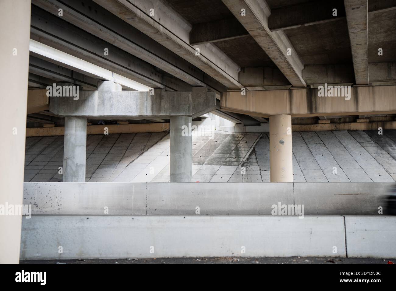 Minimal transport scene under a multilane overpass where raw concrete forms create rhythm, depth and a powerful metropolitan engineering backdrop Stock Photo