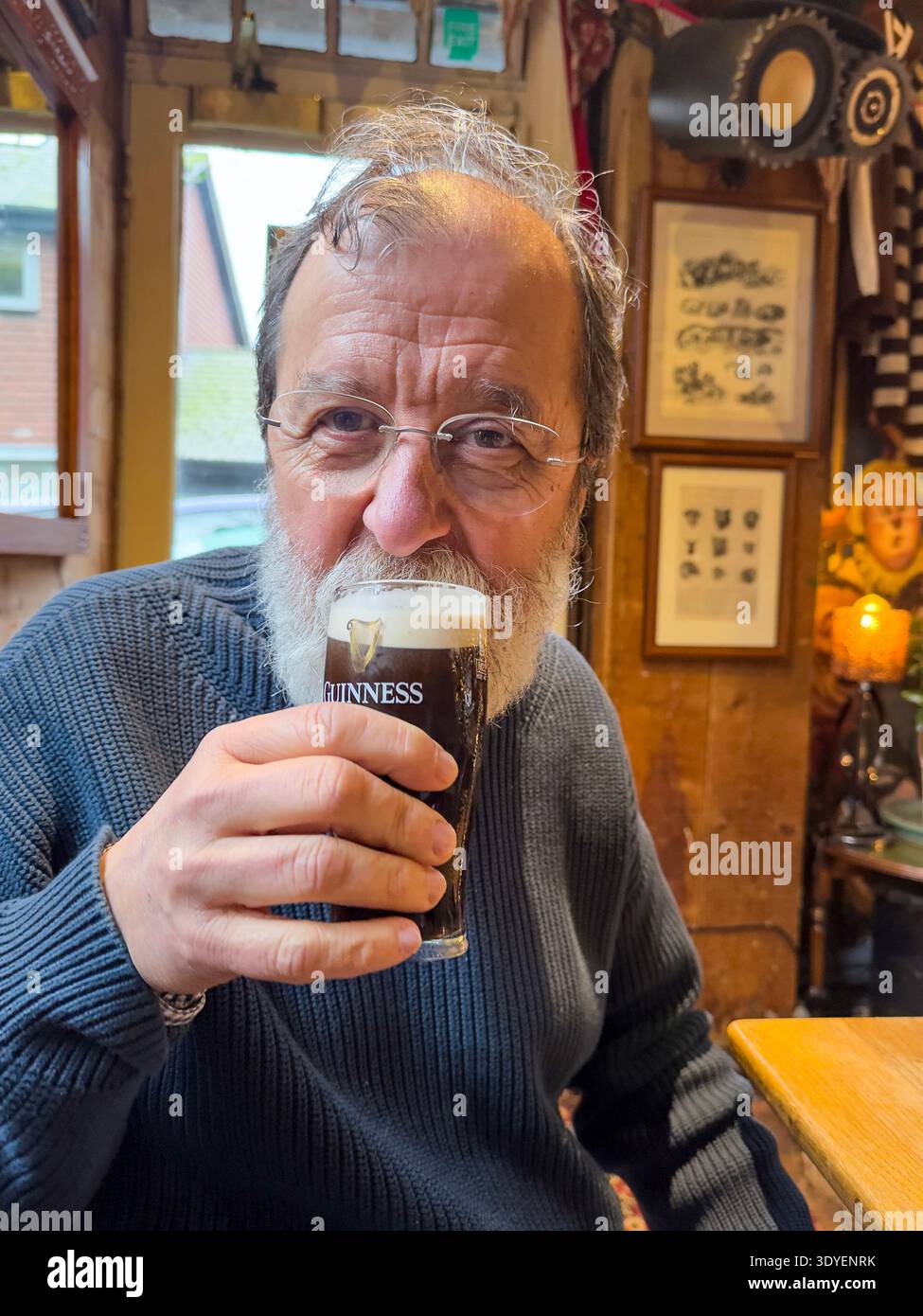 Mature man drinking a half pint of Guinness in a pub in The Snowdrop Inn, Lewes,  county town of East Sussex, England, UK - Smartphone Captured Stock Image