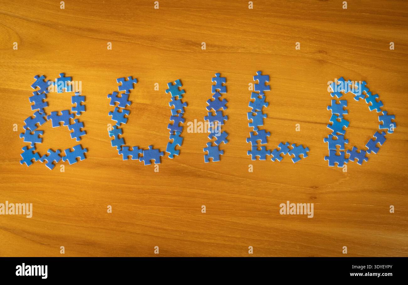 Build concept written with blue puzzle pieces arranged on a wooden table. Conceptual representation of building ideas, business development, teamwork, Stock Photo