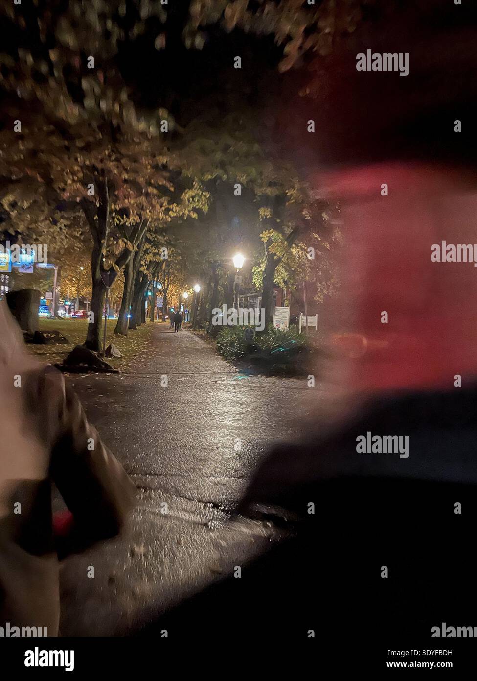 Eine Frau wird von einem Mann auf einer wenig beleuchteten Straße bei Nacht verfolgt Stock Photo