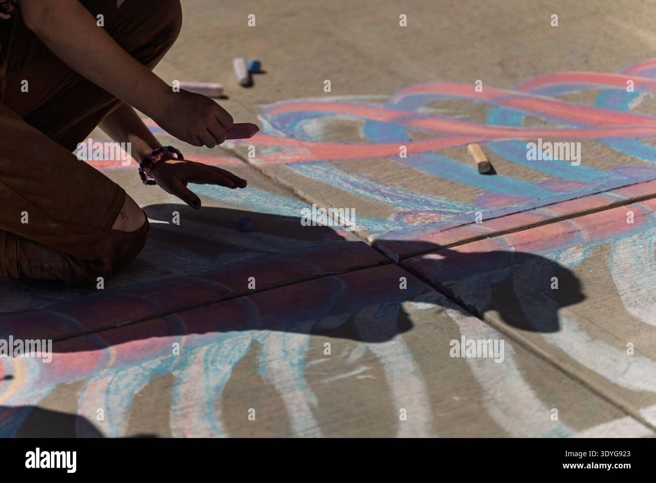 An artist kneels to create a large, colorful chalk drawing on the ...