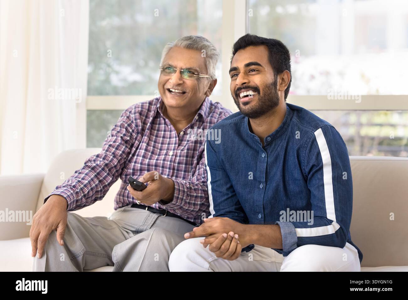 Elderly man and grownup son sitting on couch watching television Stock Photo